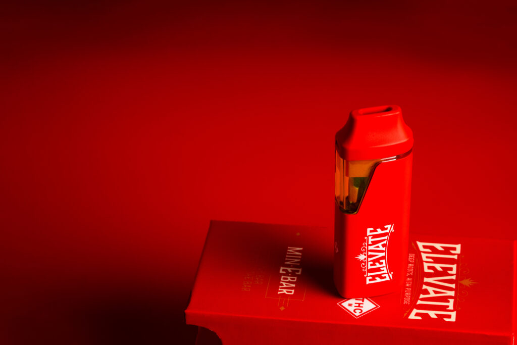 Red Min-E Bar vape resting on a box with red background