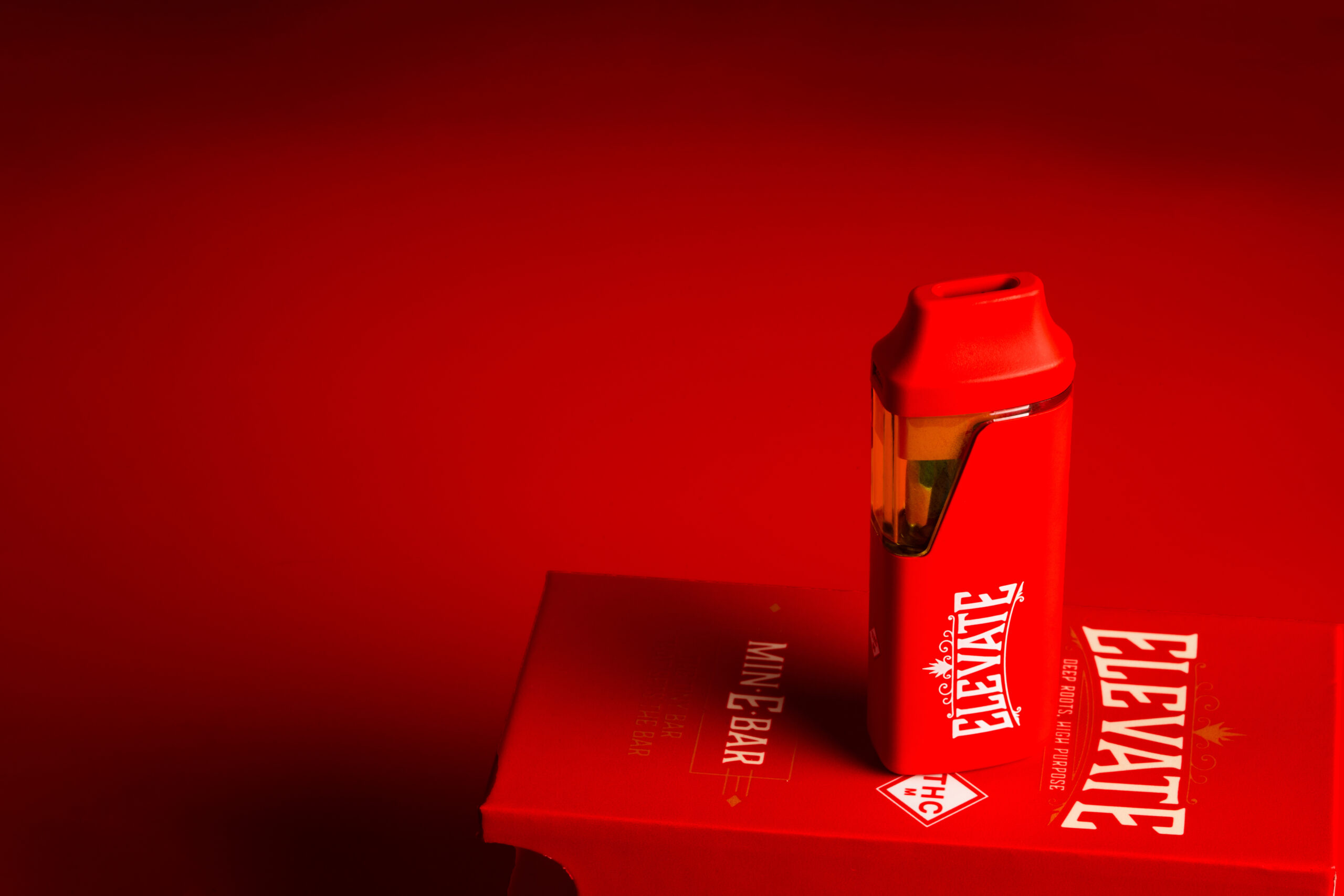 Red Min-E Bar vape resting on a box with red background